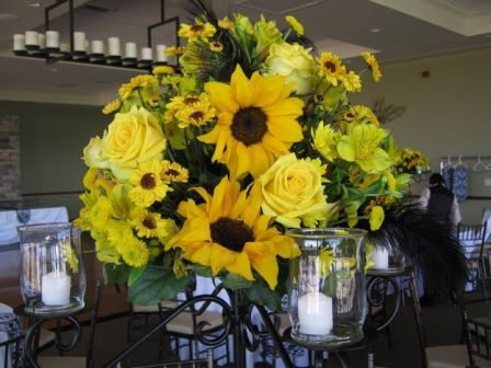 Centerpieces on top of black candelabras made of sunflowers yellow roses 